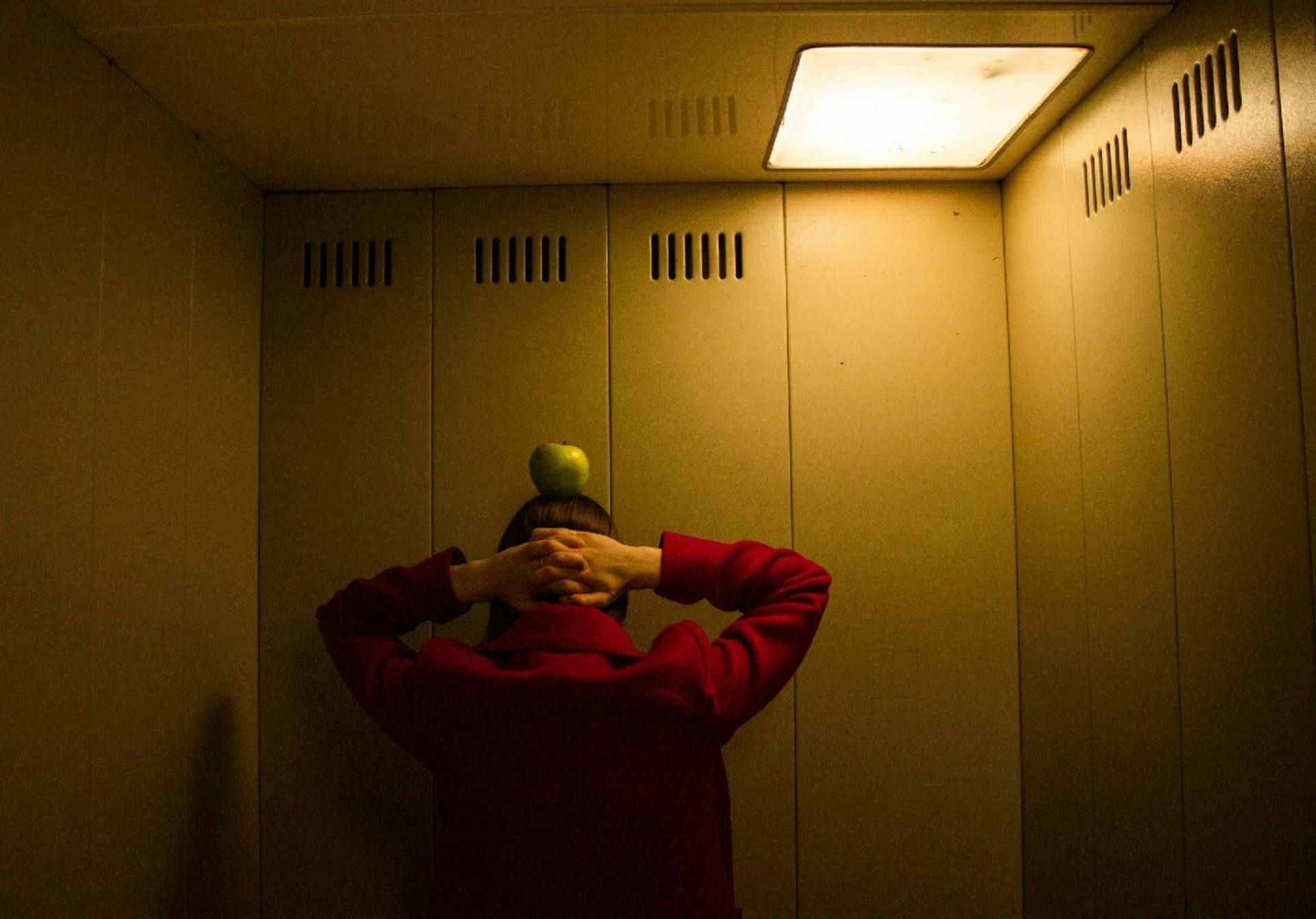 A Woman in the Elevator with Green Apple on Head