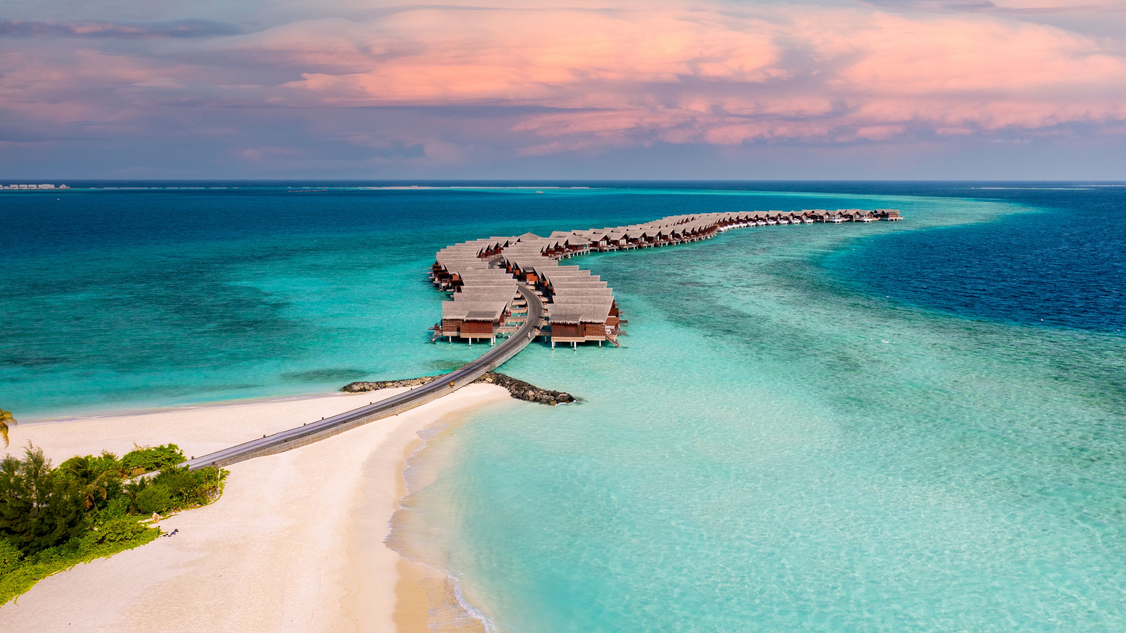 Idyllic Maldives resort with overwater villas and turquoise seas, captured at sunset from above.