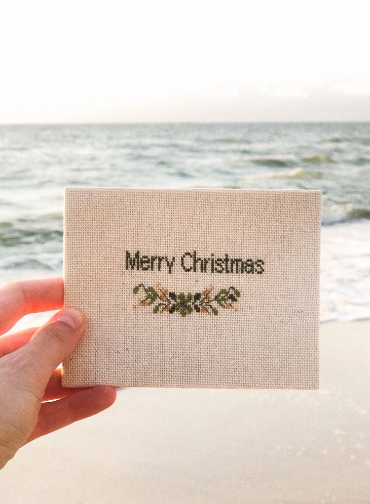 A Person Holding A Christmas Card On A Beach