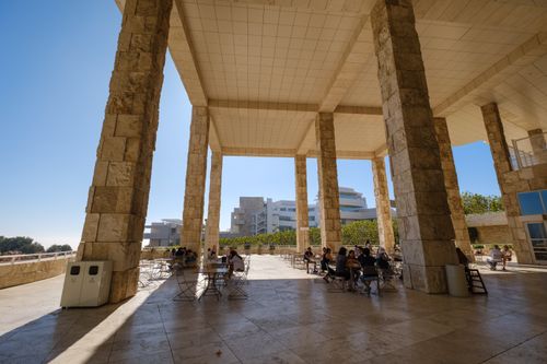 Free Outdoor terrace with people sitting under tall stone columns, clear sky, and modern architecture. Stock Photo