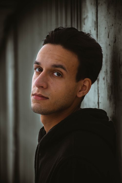 Free Portrait of a young man wearing a hoodie, leaning against a concrete wall with a moody expression. Stock Photo
