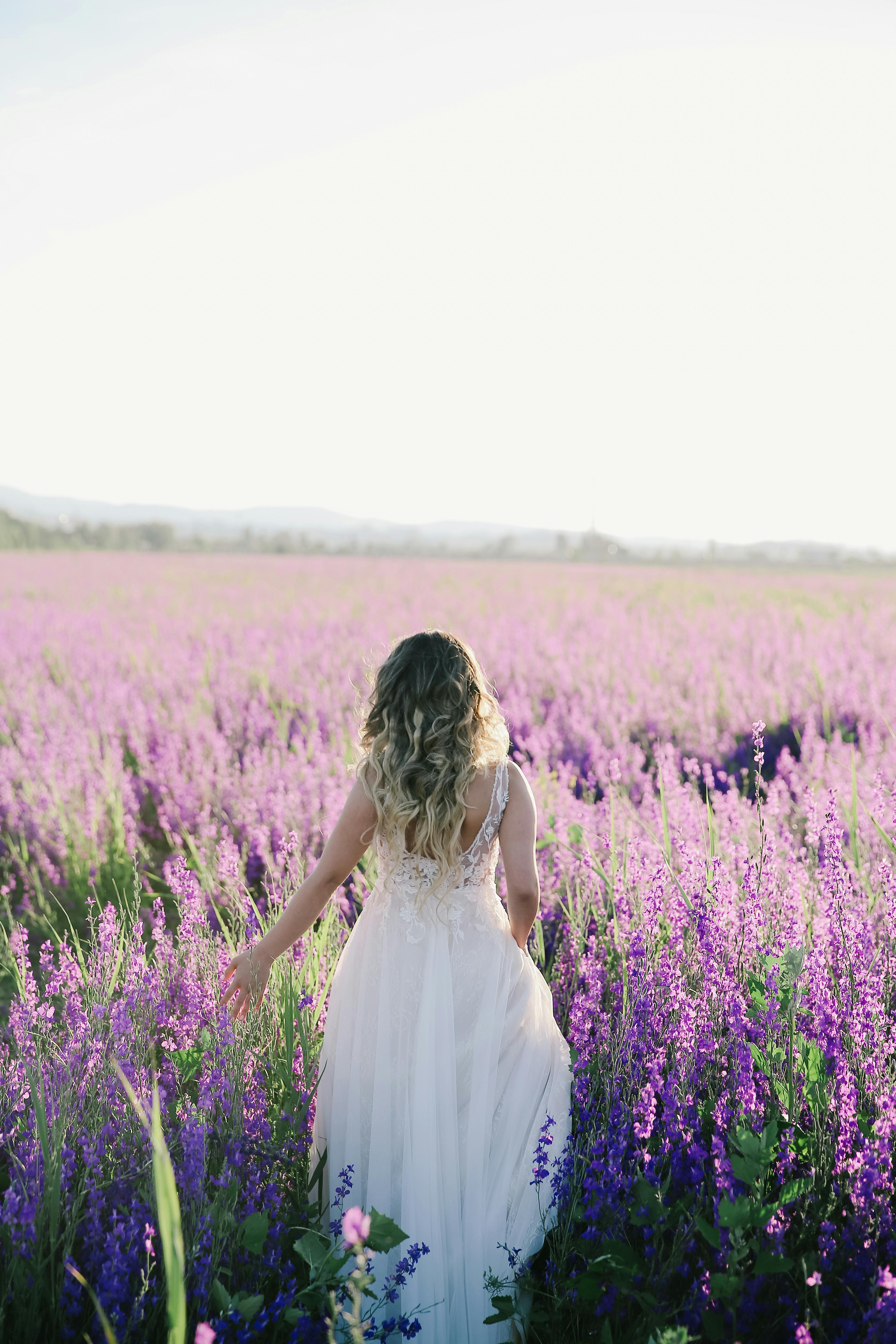 A bride in a white dress walks through a lavender field bathed in sunlight.