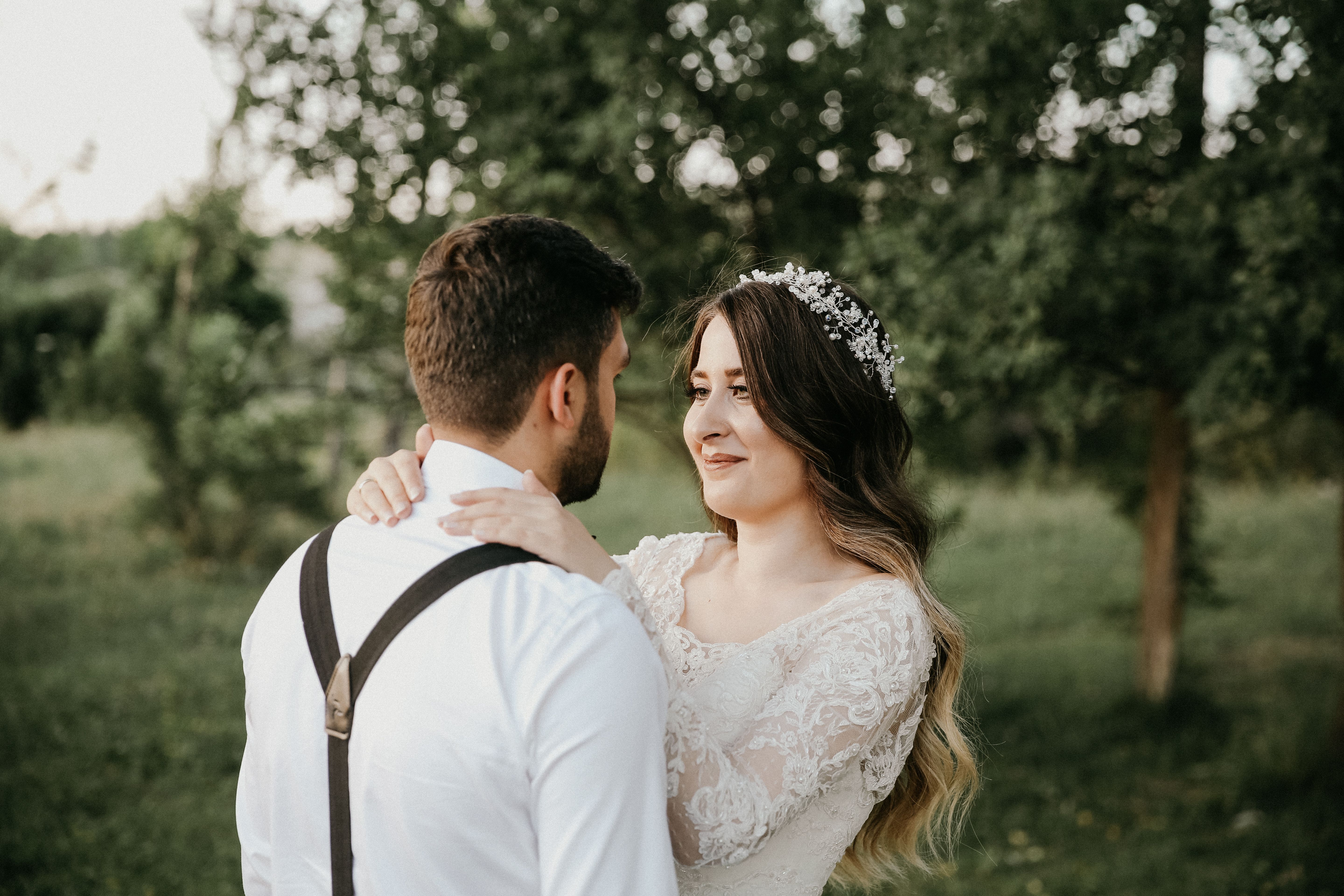 styled flat lay on a cream linen surface showing wedding hair accessories - a pearl cluster hair comb, two crystal-tipped pins, a short birdcage veil on its comb, dried lavender sprigs, and a folded i