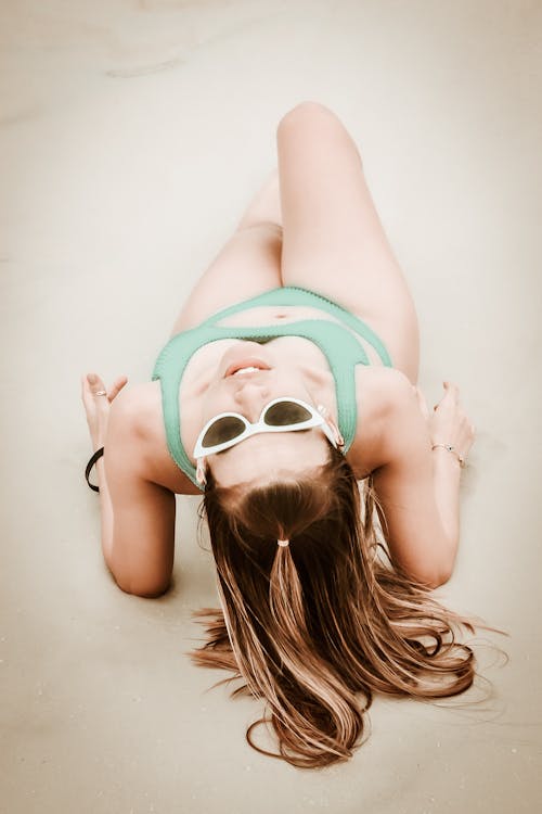 Free A Woman in Green Bikini Lying on the Beach Sand while Wearing Sunglasses Stock Photo