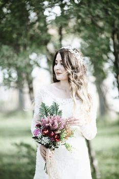Elegant bride with floral crown holding a bouquet, captured in a serene outdoor setting.