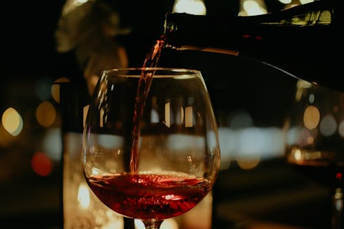 A Person Pouring Red Wine on a Clear Glass