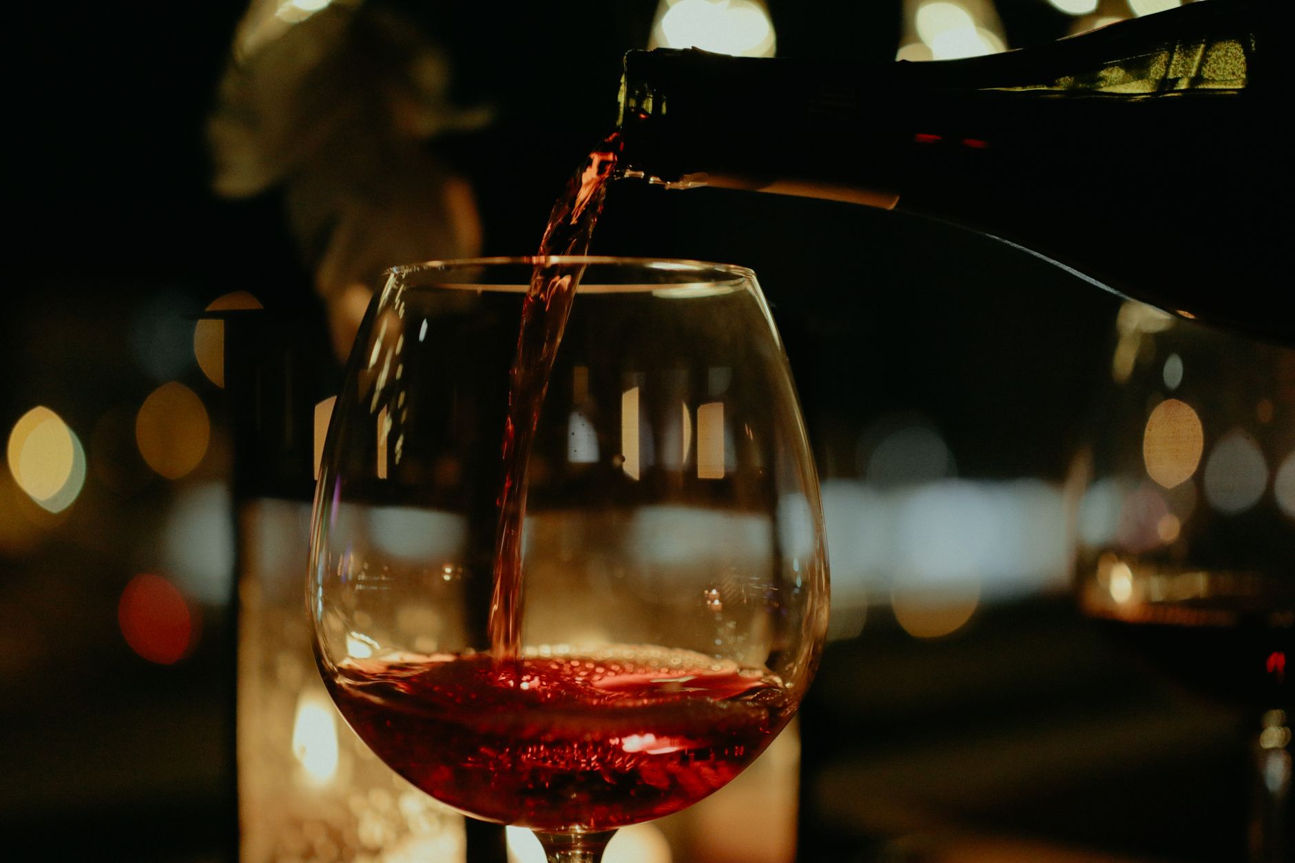 Close-up of natural wine being poured into a glass at a candlelit table with soft bokeh background.