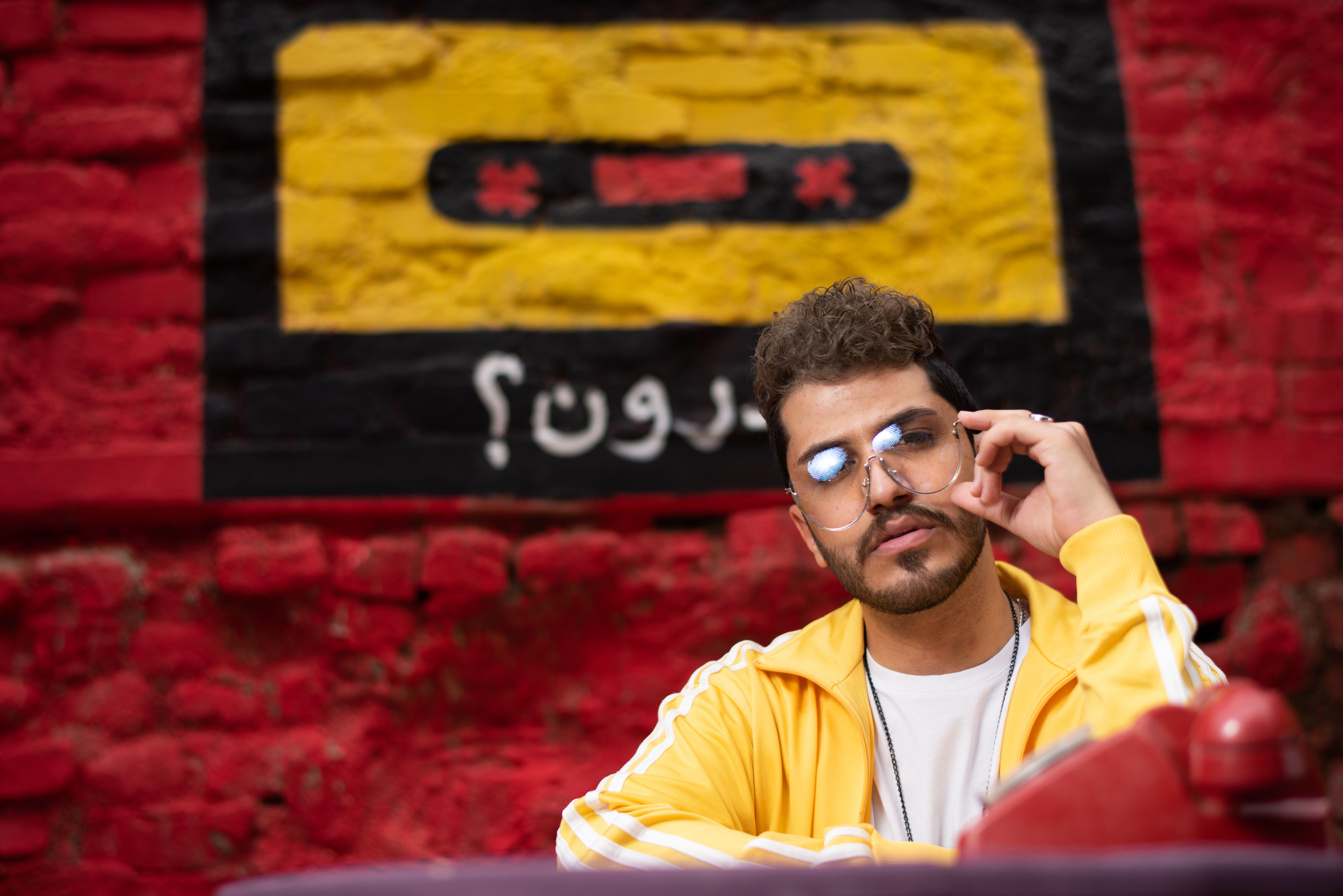 Portrait of a man in a yellow jacket posing against a vibrant graffiti wall with red and yellow colors.
