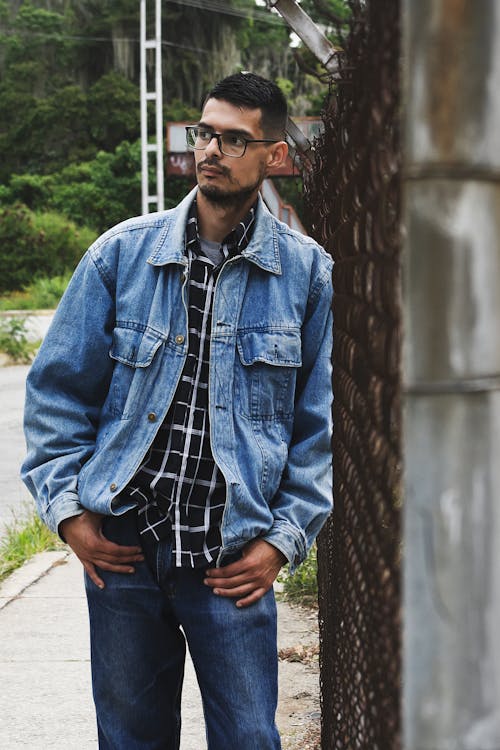 A Man in Denim Jacket Leaning on a Chain Link Fence