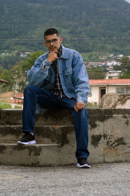 Free Man in denim jacket and jeans sitting on stone steps outdoors, thoughtful pose Stock Photo