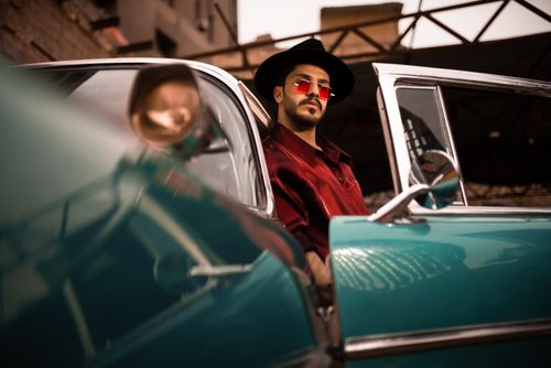 Free A fashionable man in a red shirt poses in a classic car, exuding a cool vintage style. Stock Photo