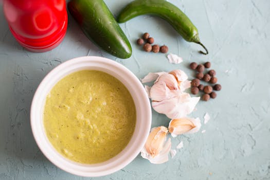 Delicious green soup with garlic cloves and jalapeños in a bowl on a textured blue background.