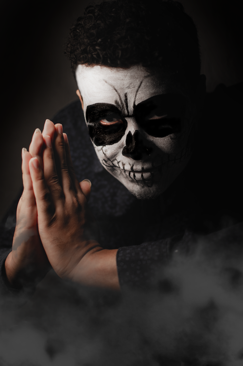 Free Dramatic portrait of a man with skeletal makeup on a dark background, hands clasped in prayer. Stock Photo