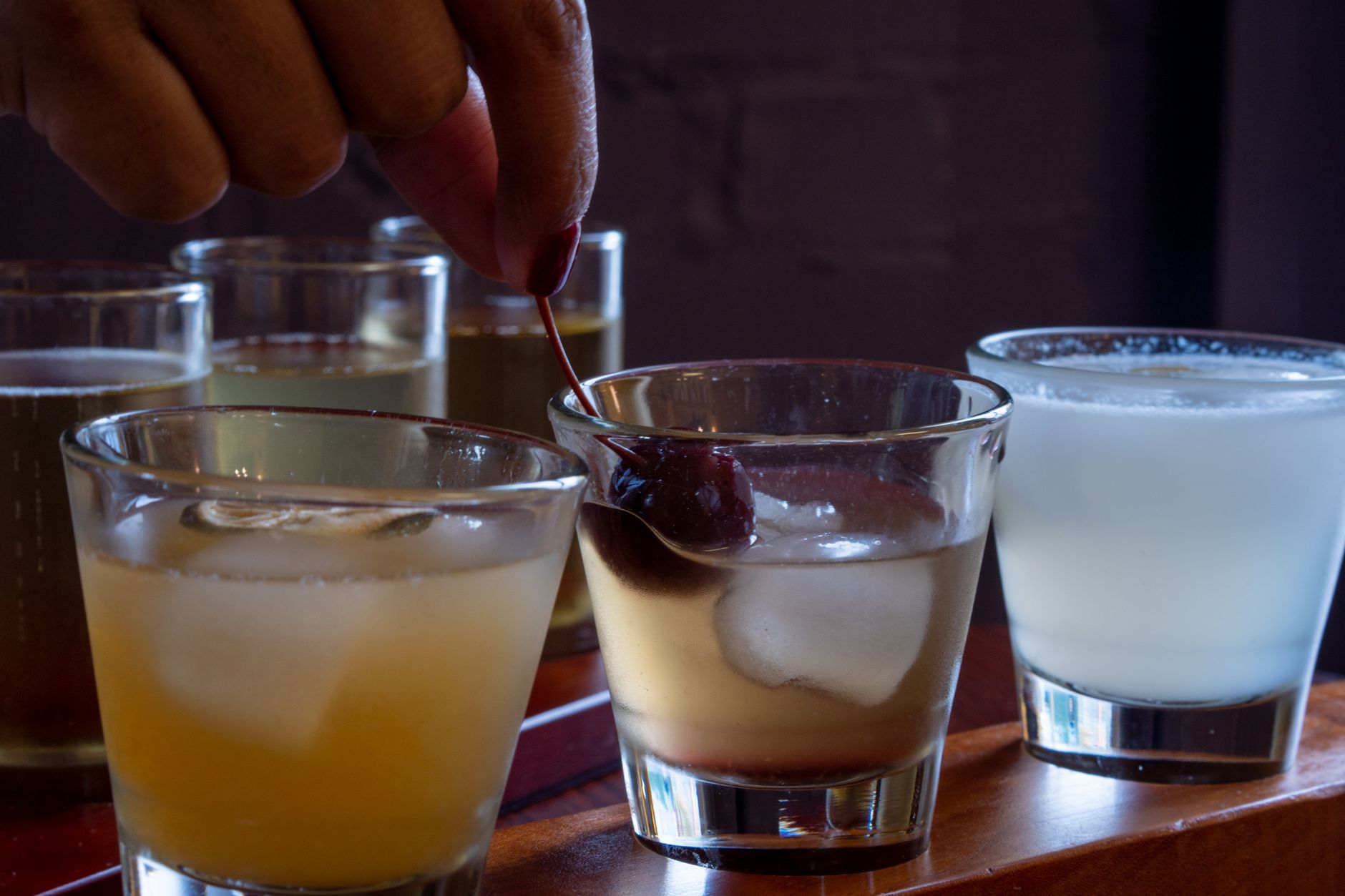 Close-up of several cocktails on a tray with a hand placing a cherry garnish