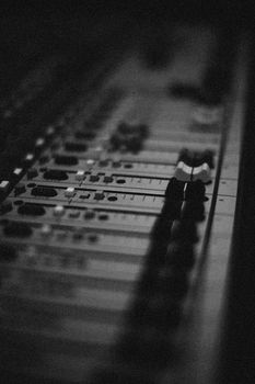 Close-up shot of an audio mixer showing knobs and faders with a blurred background and selective focus.