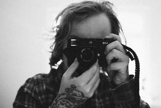 Grayscale image of a tattooed photographer holding a camera close-up.