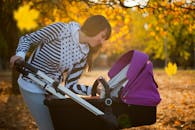 在公园散步的秋天，一位母亲低头对着婴儿车里的孩子微笑
