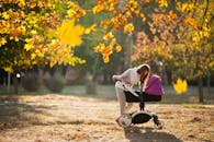 在阳光明媚的秋季公园里，母亲推着婴儿车漫步，周围是五彩缤纷的树叶