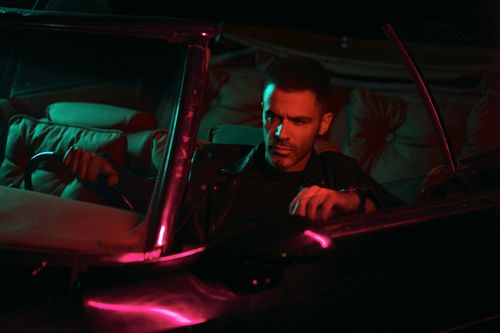 Free Man in leather jacket driving a vintage car under neon lights. Stock Photo