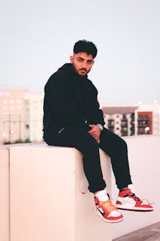 Young man in black hoodie seated outdoors, showcasing fashionable red sneakers.