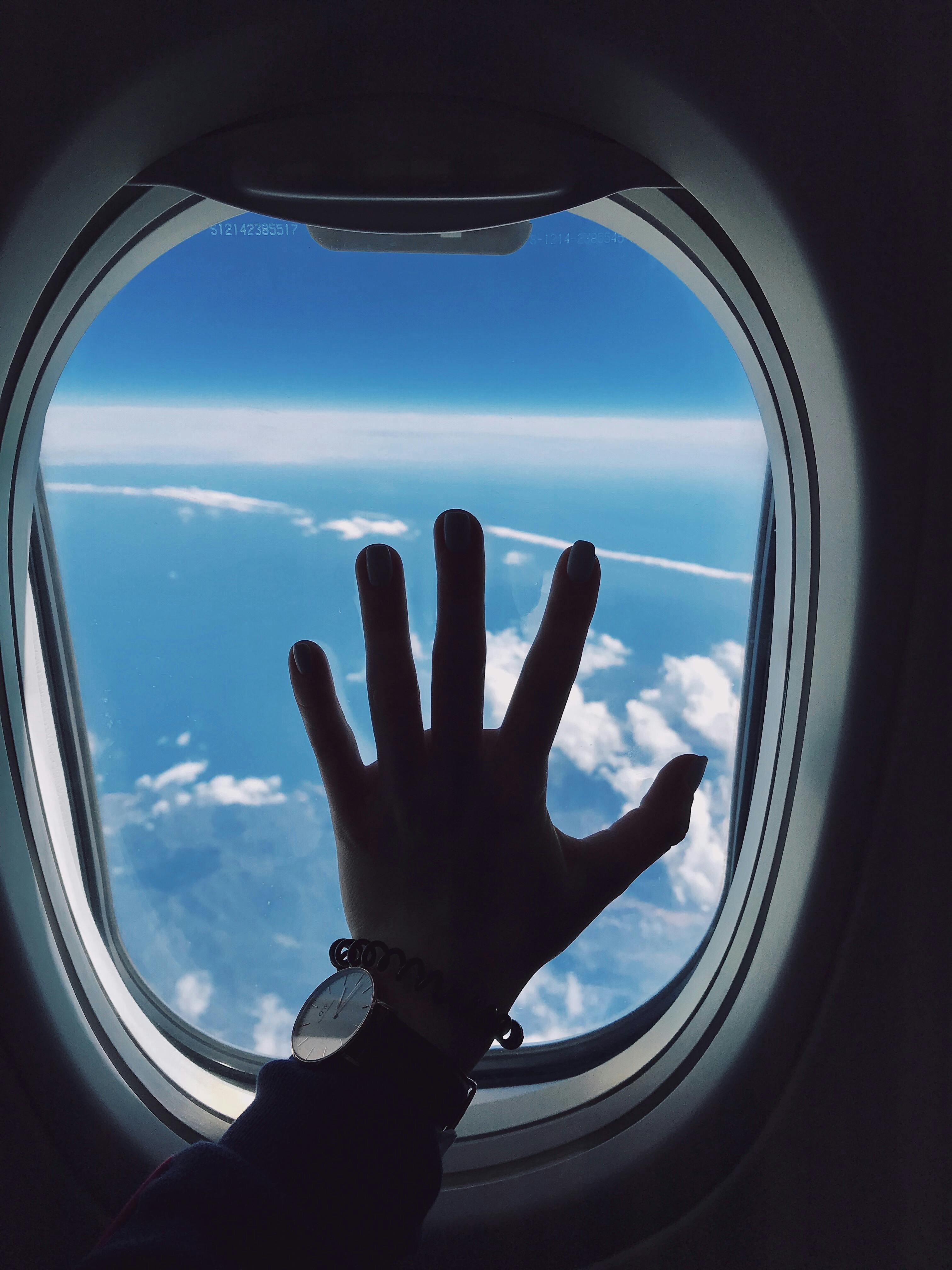 photography of person s left hand touching an airplane s window