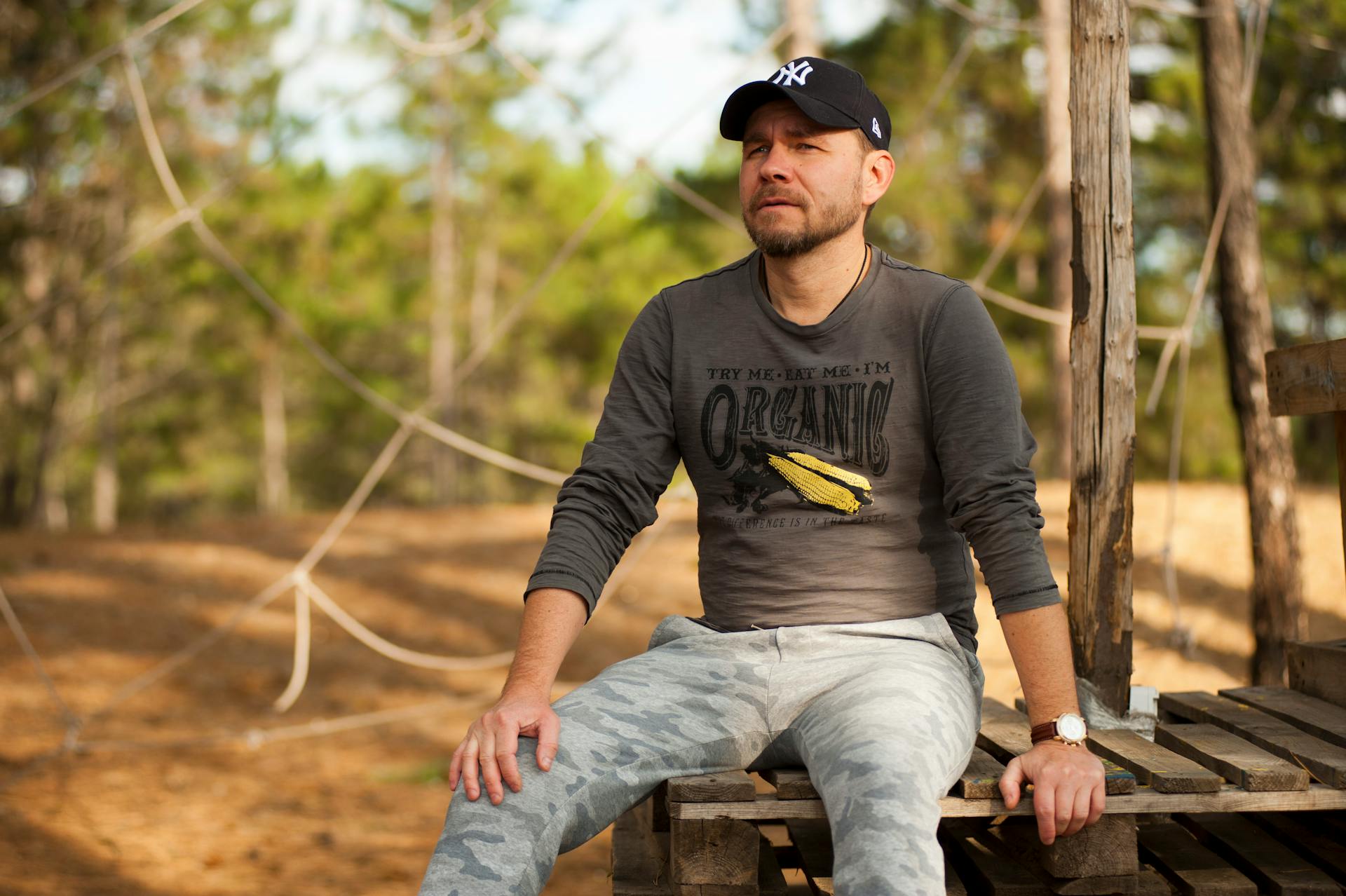 Casual man sitting on a wooden seat outdoors in the park under daylight.