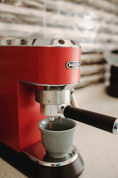 A stylish red espresso machine brewing coffee in a modern kitchen setting.