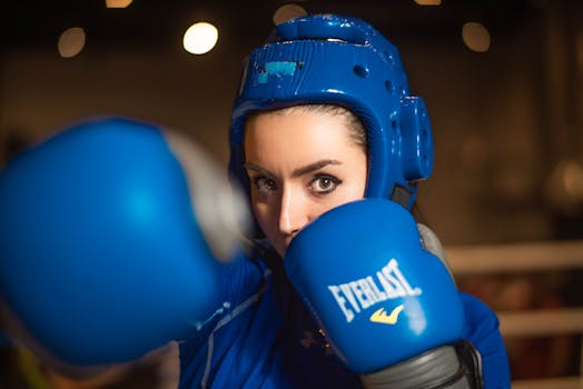 A female boxer wearing blue gear preparing to punch inside a gym.