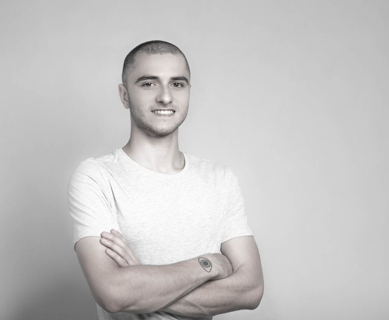 Grayscale portrait of a confident young man with crossed arms and a subtle smile.
