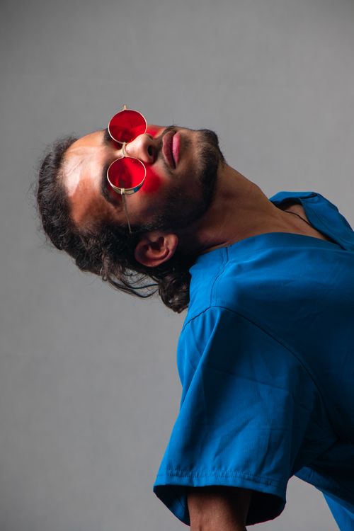 Free Stylish man wearing red sunglasses and a blue shirt poses dramatically against a gray background. Stock Photo