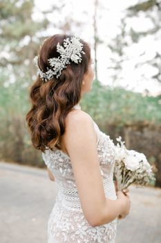 A bride in a lace wedding dress posing elegantly outdoors.