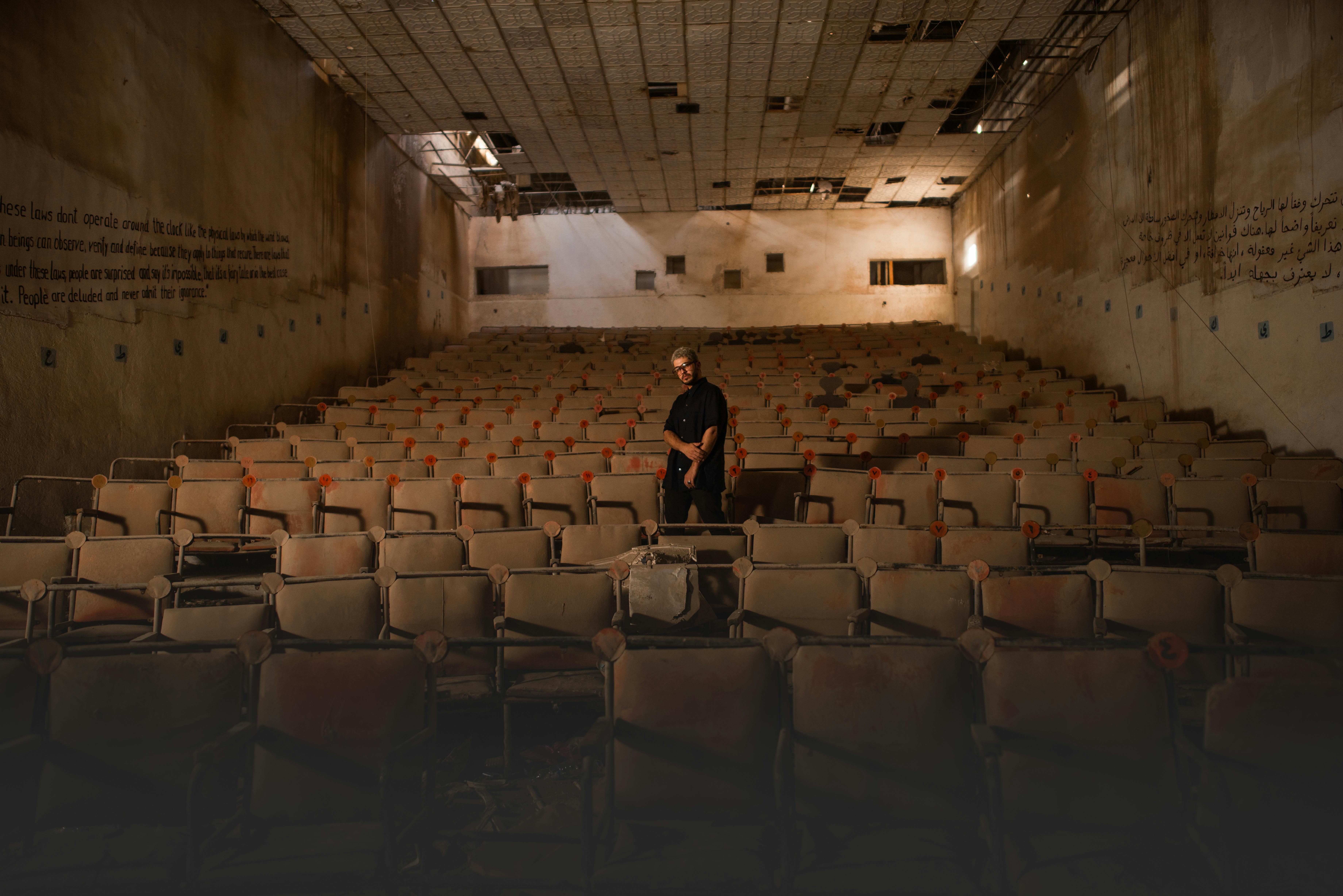 Free A lone person stands in an abandoned, decaying theater filled with broken chairs. Stock Photo