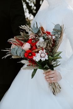 A close-up of a bride holding a stylish bouquet with red and white flowers.
