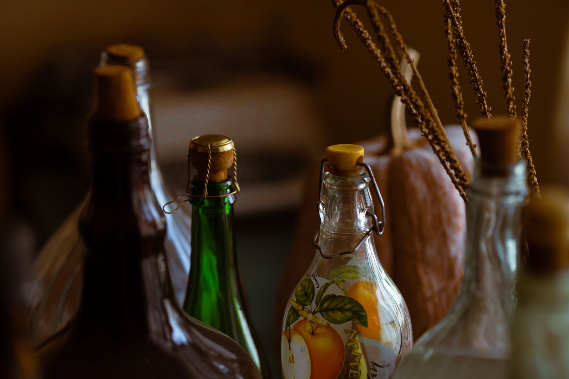 Artistic display of vintage corked bottles and glassware with warm tones and dried plants.