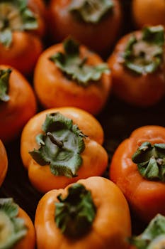 A collection of ripe orange persimmons with green leaves, perfect for autumn harvest themes.