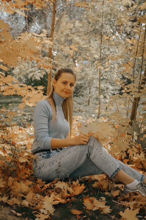 A Woman in Turtleneck Sweater Sitting on the Ground with Brown Leaves