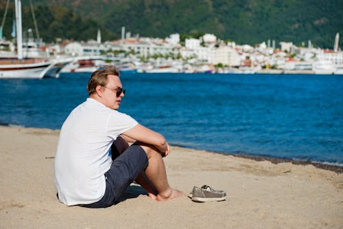 Photo of Man in White Shirt and Blue Short Sitting on Seashore