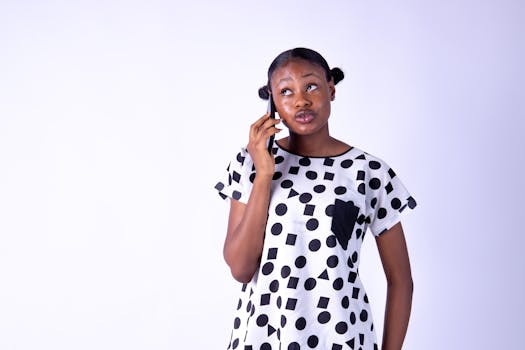 African woman engaged in a phone call against a white background, looking thoughtful.