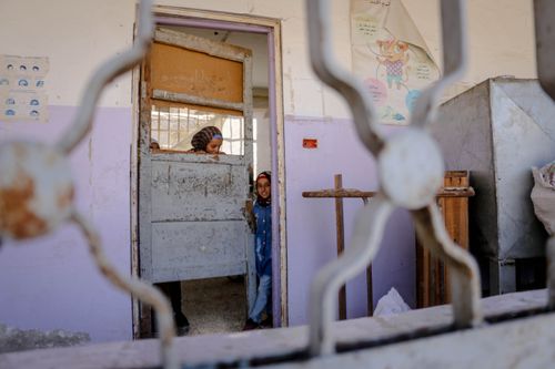 Free Two children peering through an old classroom door in a Syrian school, creating a poignant scene. Stock Photo