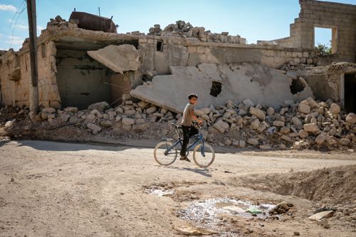 Free A boy rides a bicycle through a rubble-strewn street in war-torn Idlib, Syria. Stock Photo