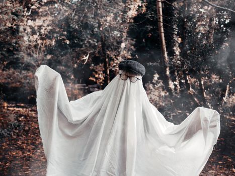 Eerie figure in ghost costume with glasses in a forest, evoking Halloween spirit.