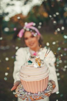 A woman holding a festive cupcake adorned with confetti in a joyful outdoor setting.