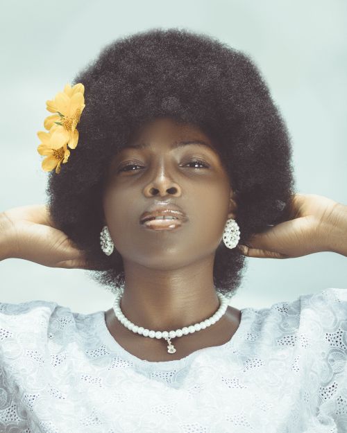 Free Close-up portrait of a woman with an afro, adorned with jewelry and a flower, posing confidently indoors. Stock Photo