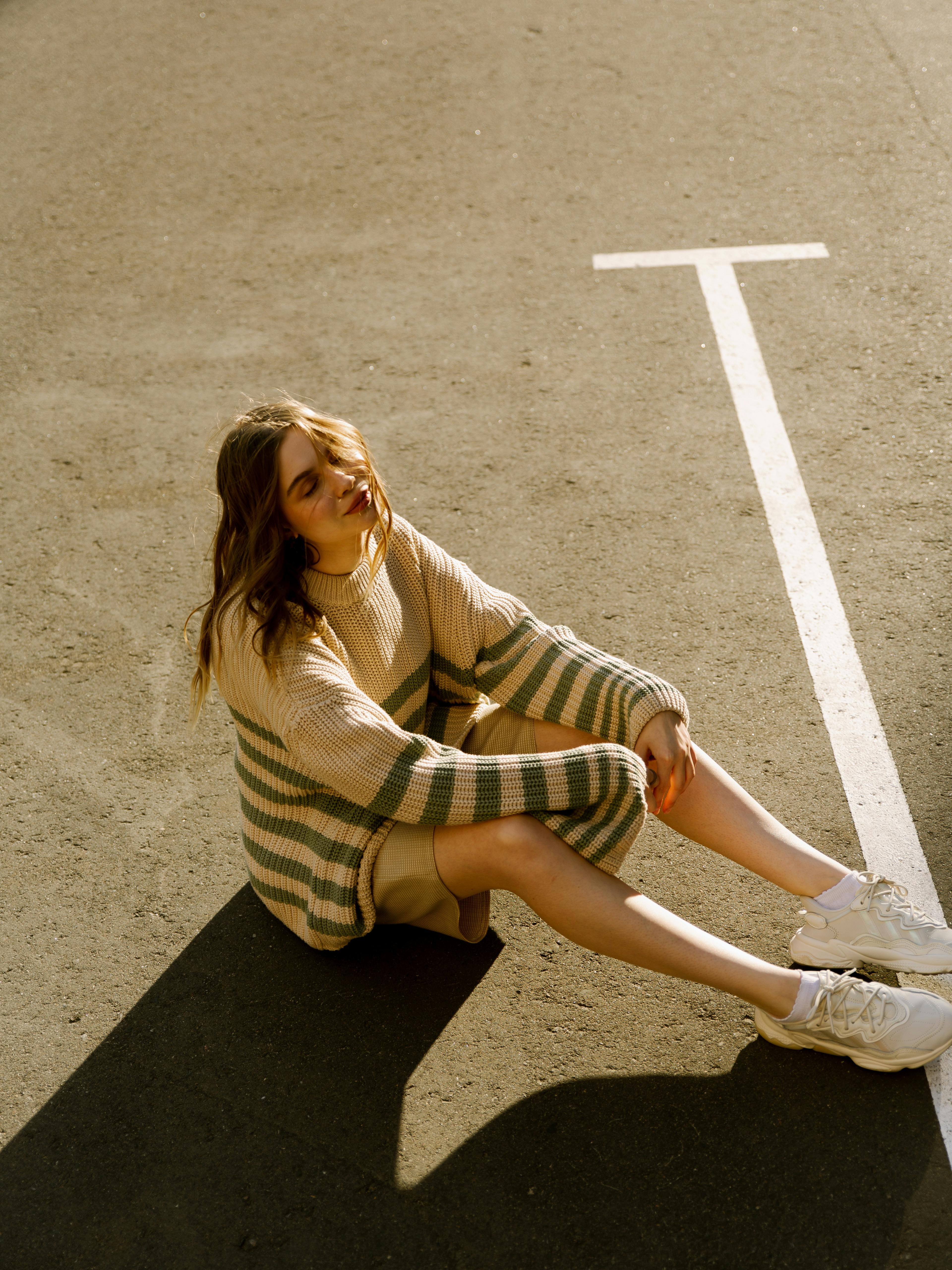 Stylish woman in a cozy sweater sitting on a sunny urban street.