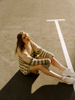 Stylish woman in a cozy sweater sitting on a sunny urban street.