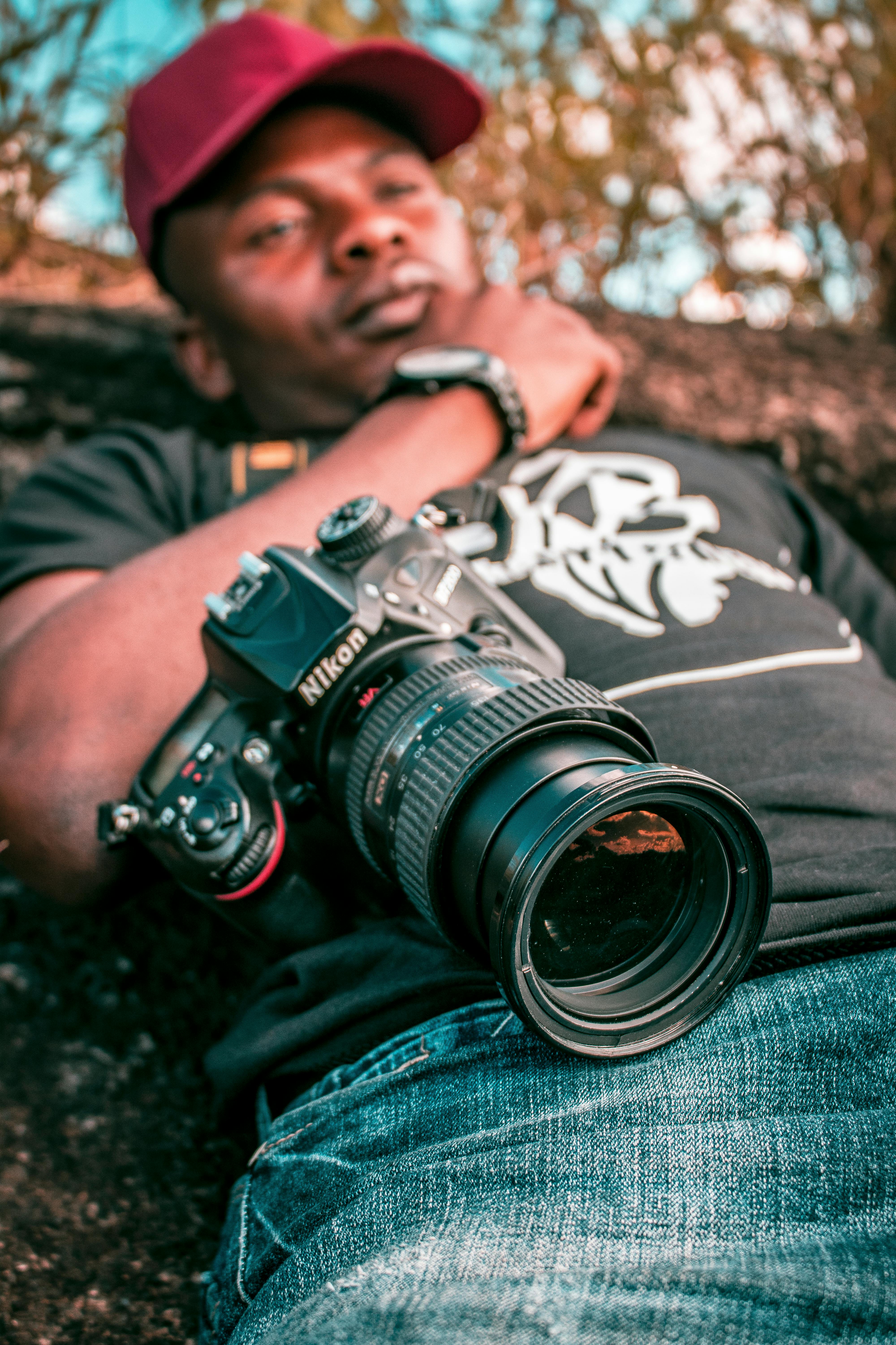 Black man lying outdoors with camera, showcasing leisure and relaxation.