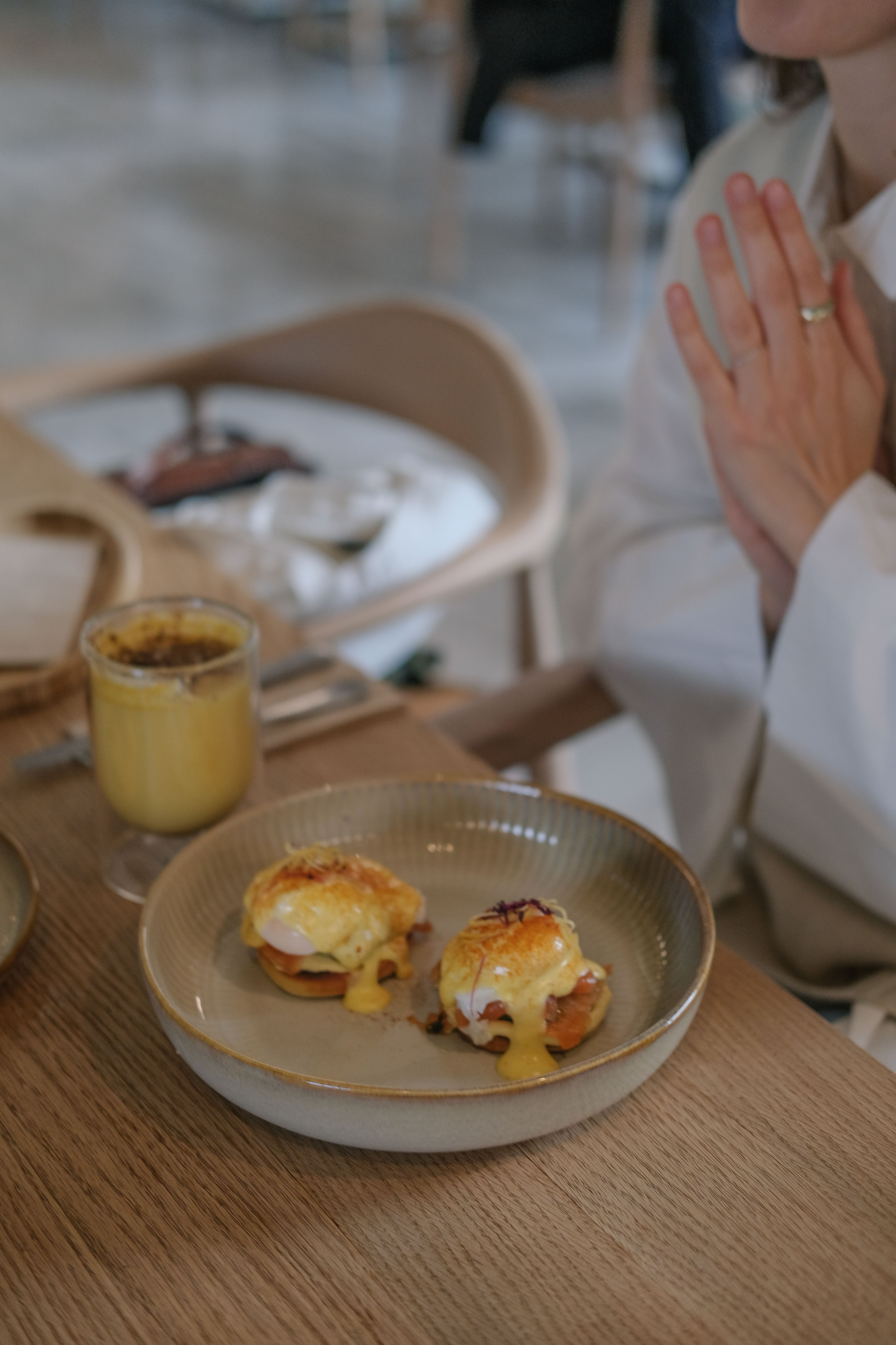 Plate of Eggs Benedict with a glass of juice on a wooden table in a cafe.