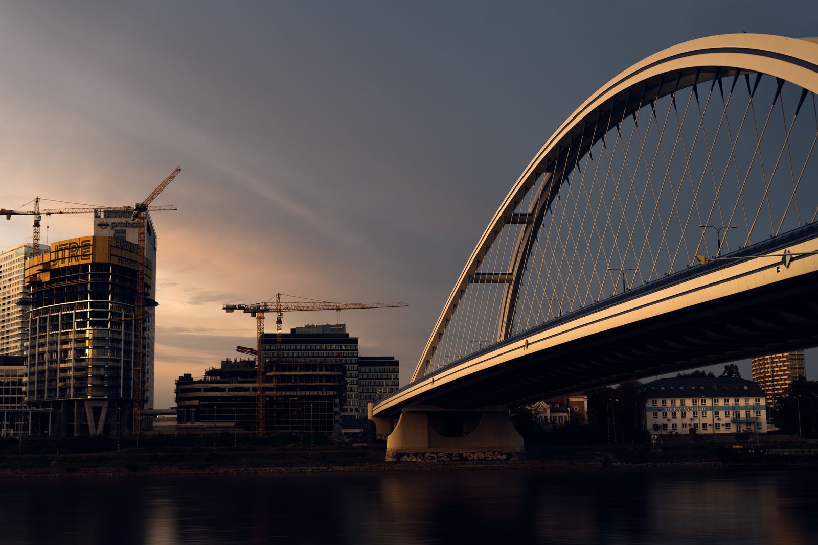 City skyline with a modern bridge and construction cranes at sunset