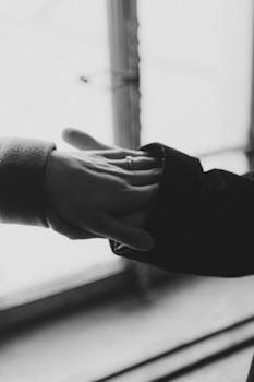 Grayscale image capturing hands holding, showcasing a ring in intimate romance.