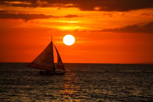 Free A mesmerizing sunset over Boracay, Philippines, silhouetting a traditional sailboat. Stock Photo